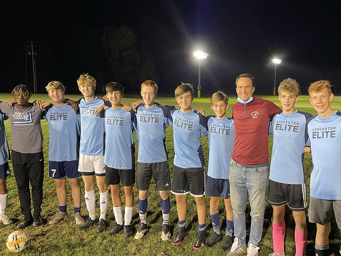 An adult in a red shirt with a group of youth soccer players in blue jerseys