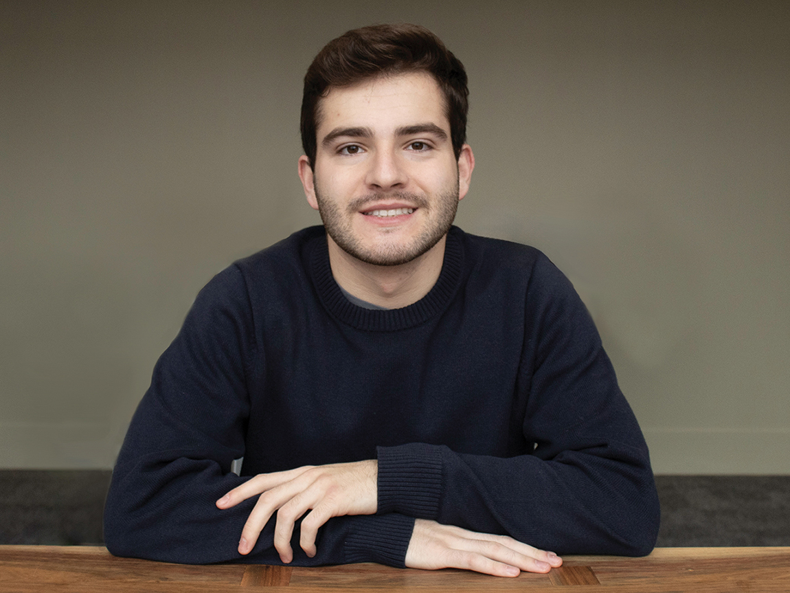 A headshot of a college student wearing a black shirt in front of a beige background