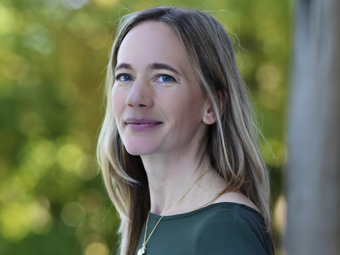 A headshot of a woman with long hair on a green background