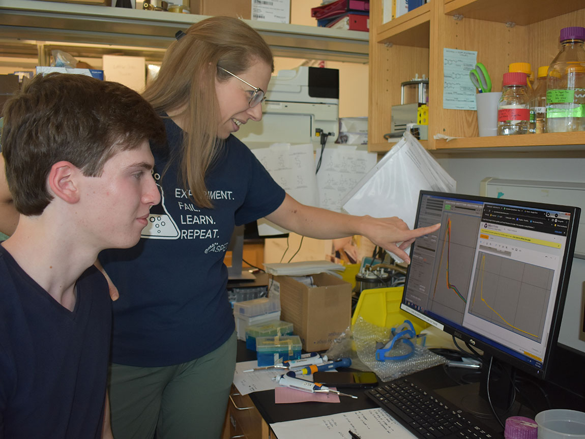 A college professor and a student look at a computer screen together in a chemistry lab