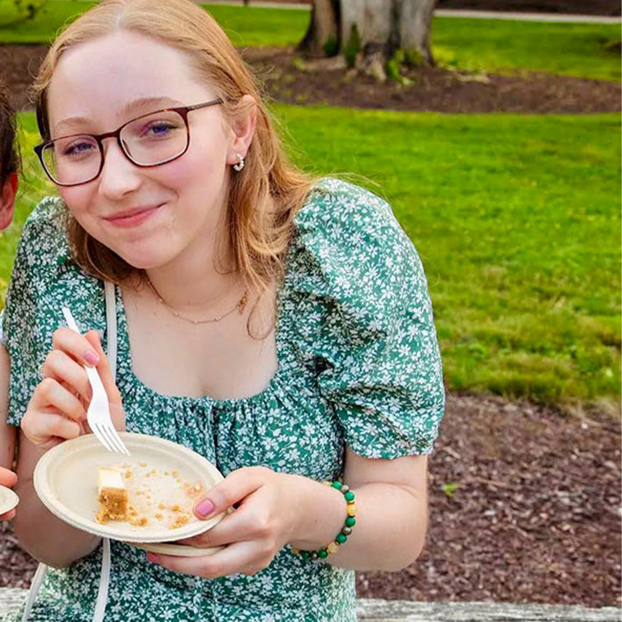 A young adult holds a plate of cake and smiles at the camera.