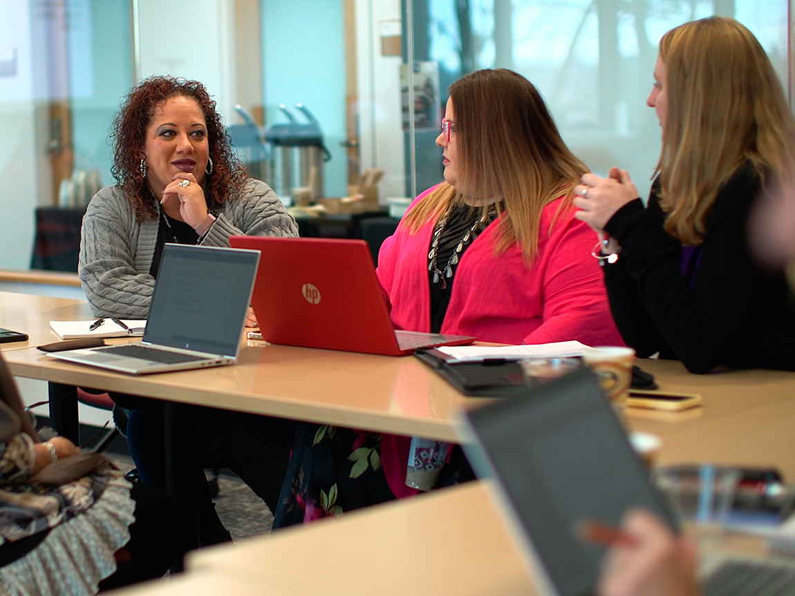 Students in the diversity, equity, inclusion and belonging graduate certificate program have a discussion at a table with their laptops open