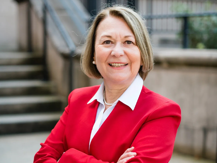 A woman with short blonde hair and a bright red blazer smiles at the camera.