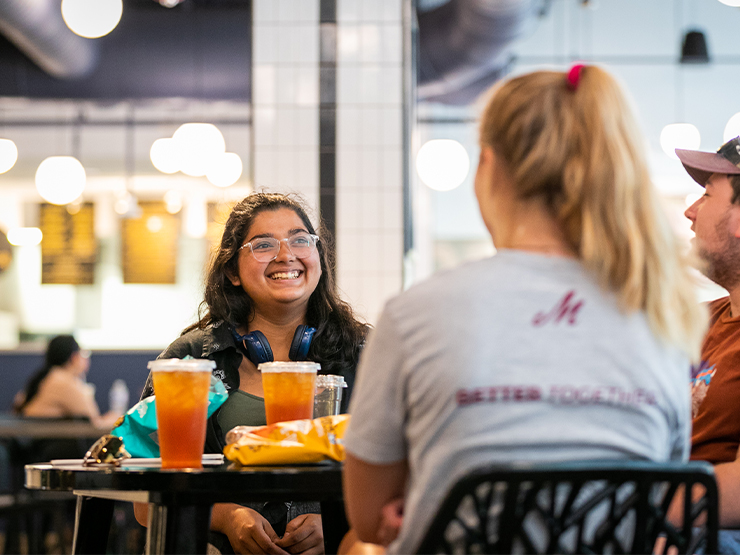 Young adults smile around a table of drinks and food in a restaurant.