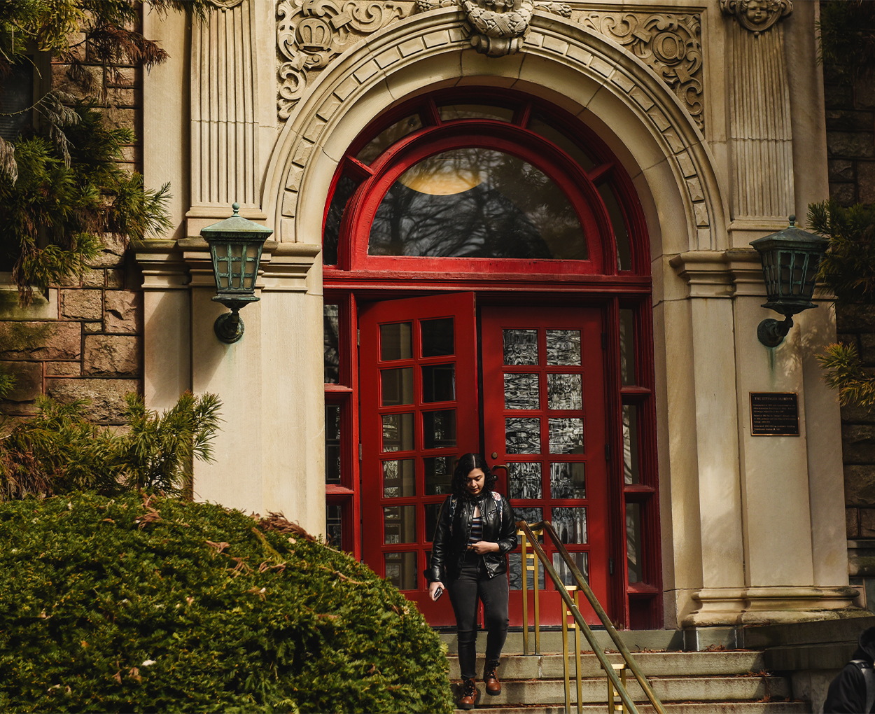 A student walks out of a pair of red doors in a college building.